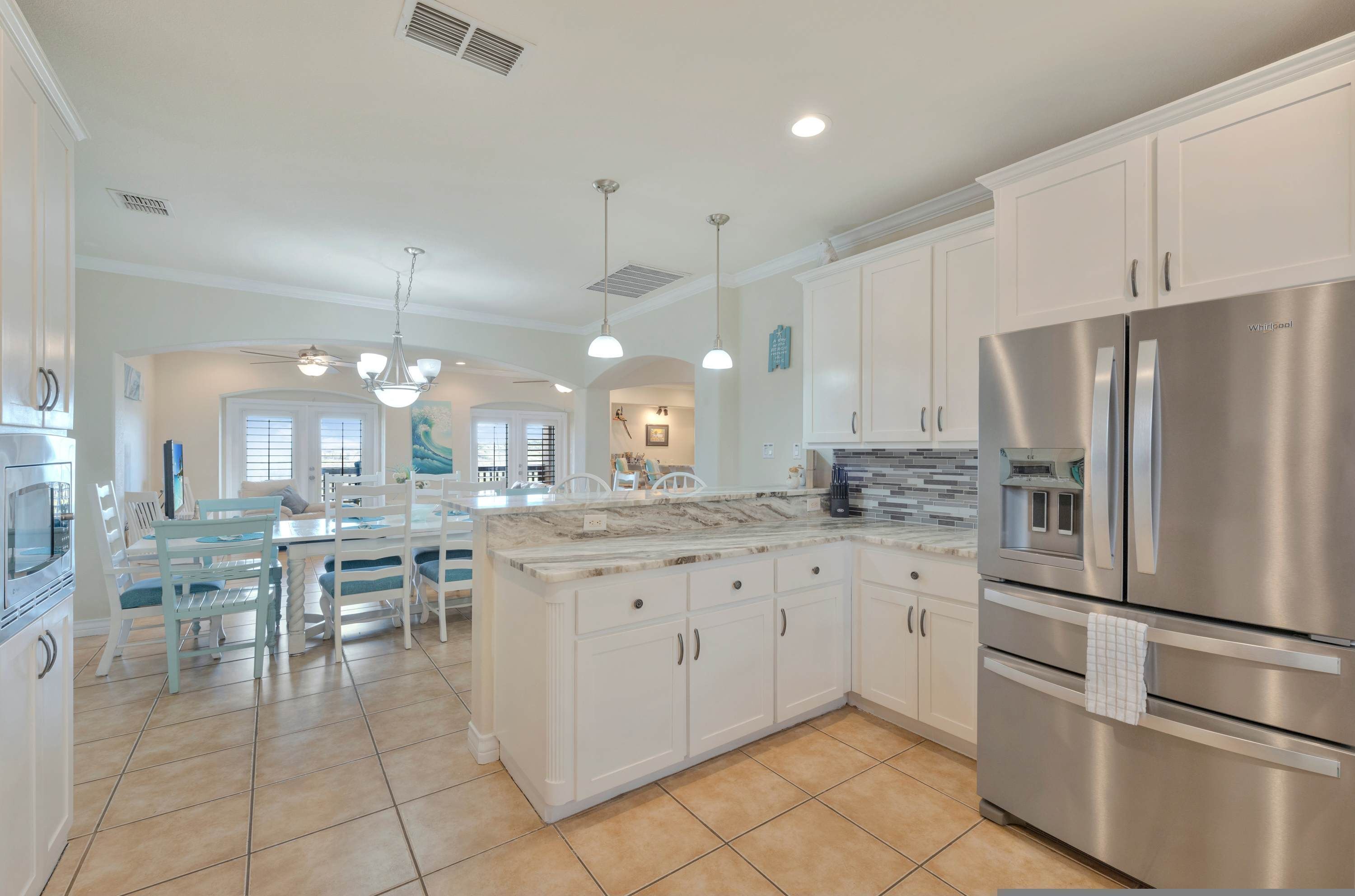 A modern kitchen with white cabinetry, a stainless steel refrigerator, and a marble countertop.