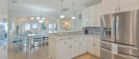 A modern kitchen with white cabinetry, a stainless steel refrigerator, and a marble countertop.