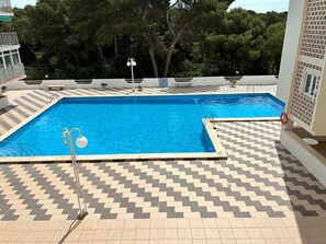 Ein Schwimmbecken mit einem Zickzack-belag, umgeben von Bäumen und einem Gebäude mit einem Balkon.