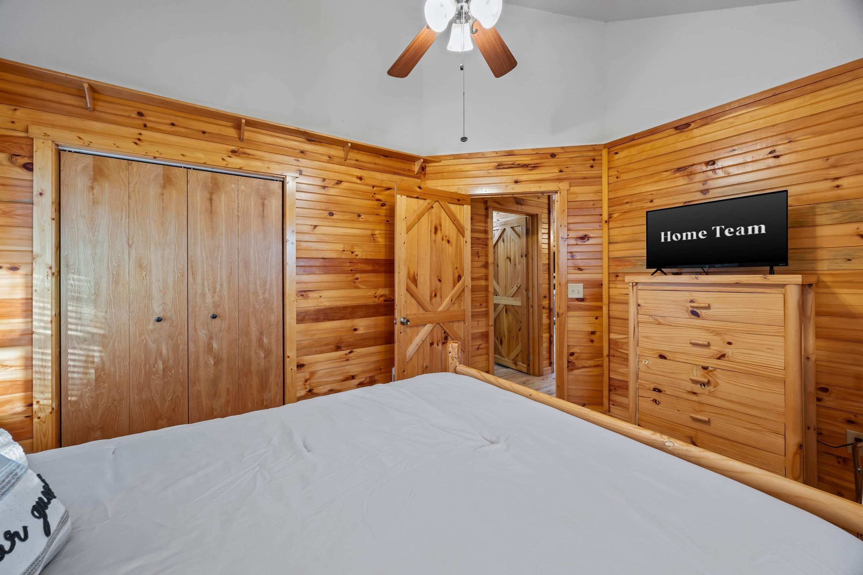 A bedroom with wooden paneling, a bed, a television, and a ceiling fan.