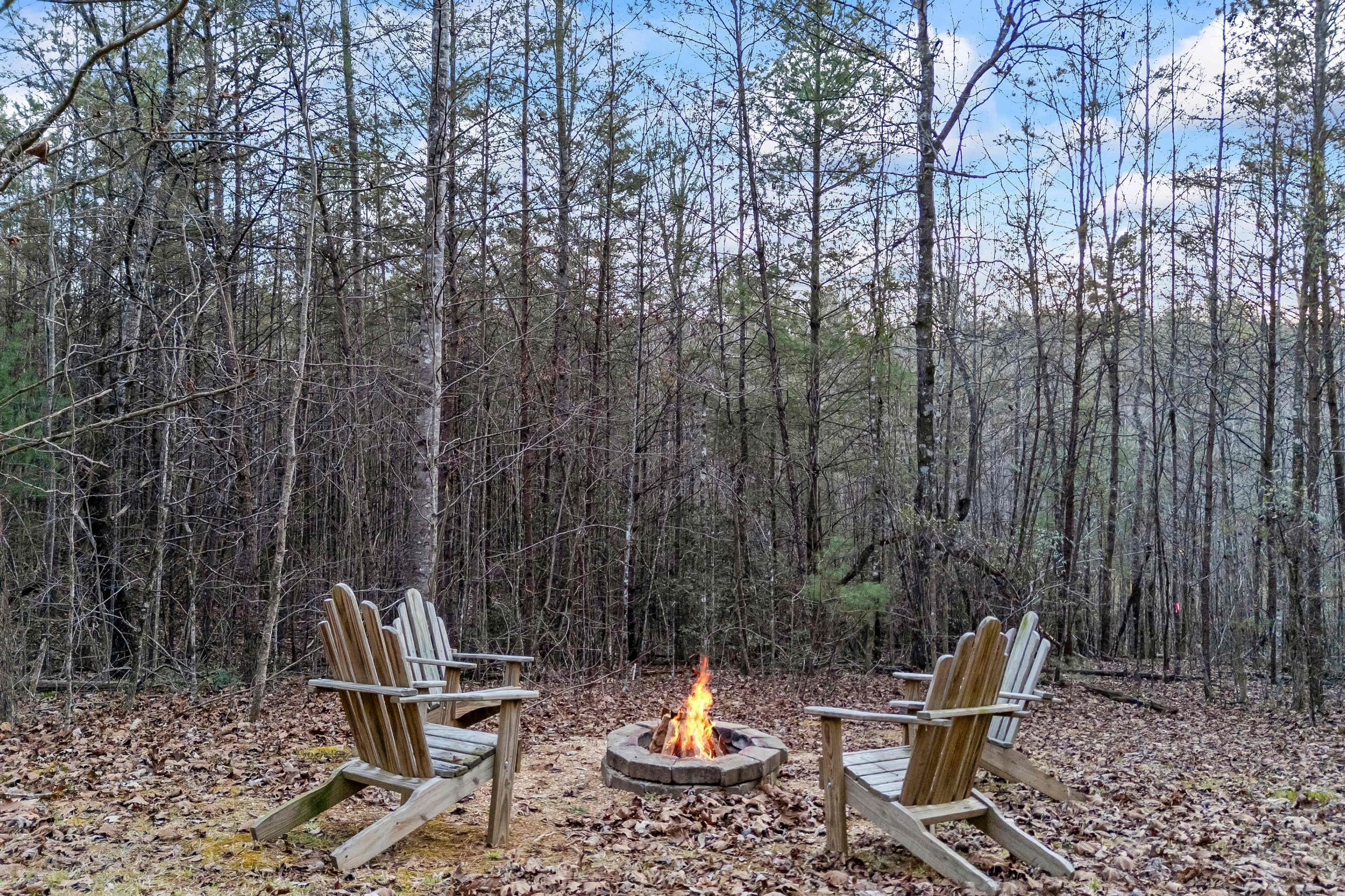 Two wooden chairs facing a campfire in a forest.