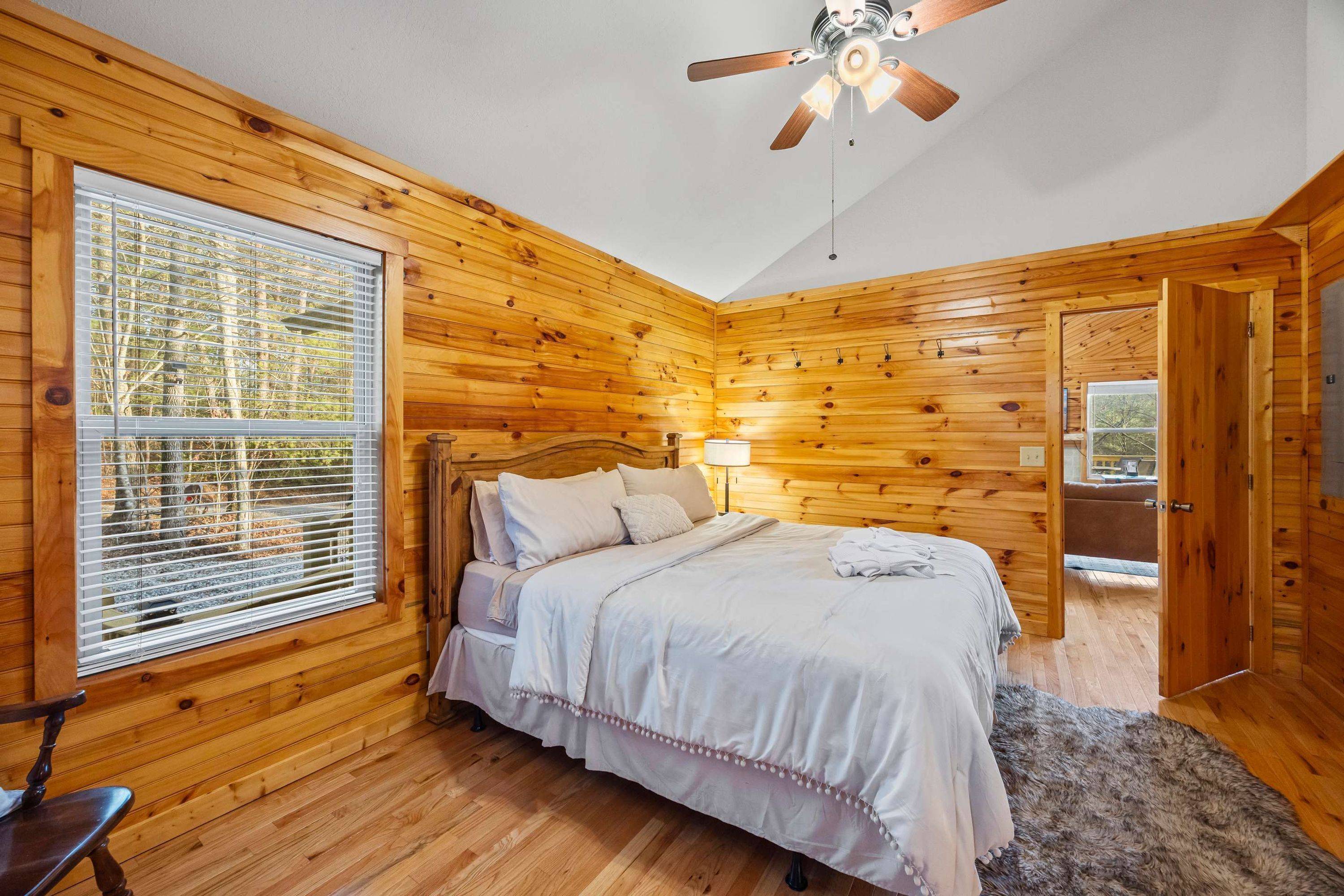 A wooden-paneled bedroom with a bed, a ceiling fan, and a window with blinds.