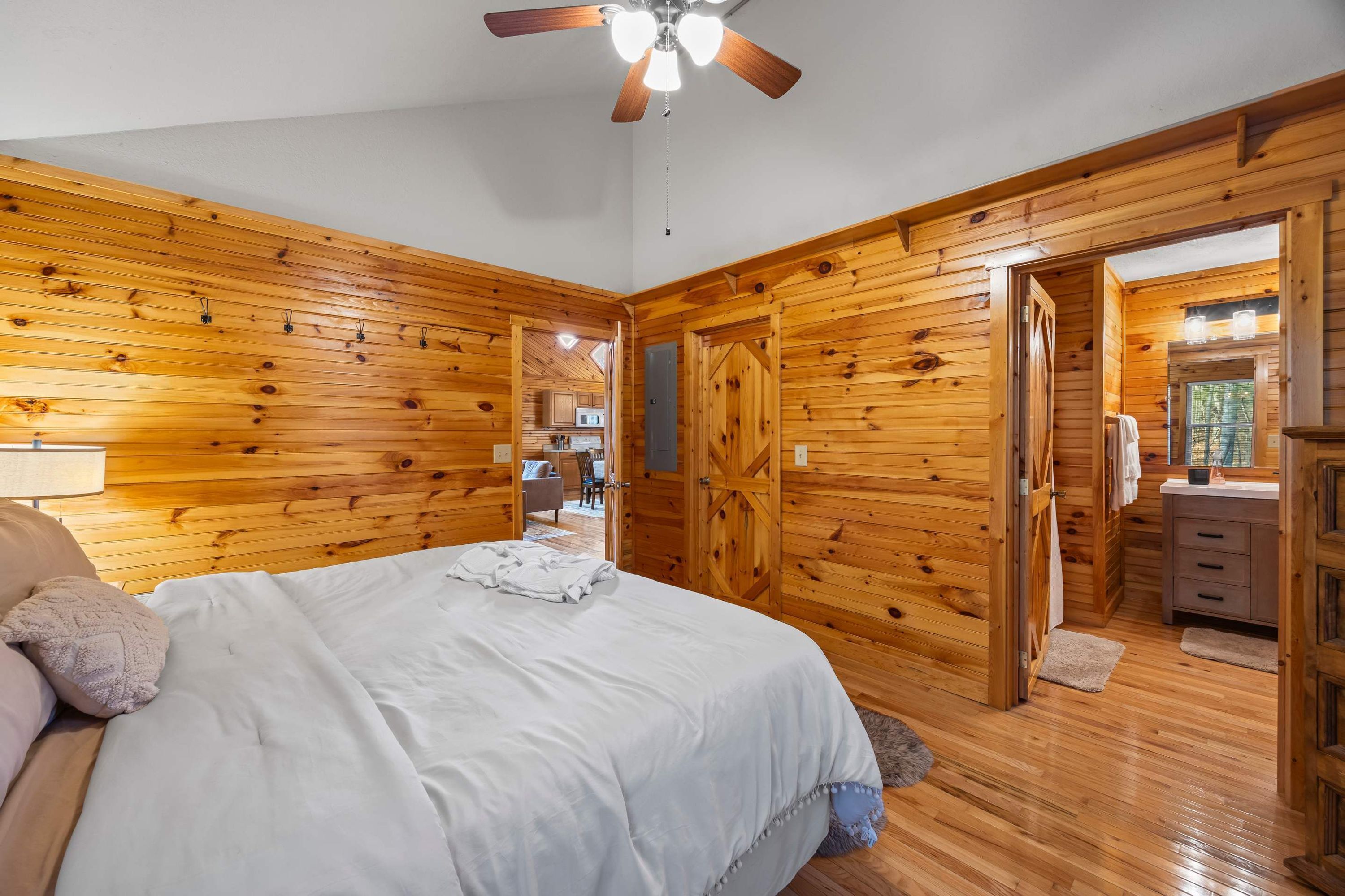 A wooden-paneled bedroom with a bed, a ceiling fan, and a view into a bathroom.