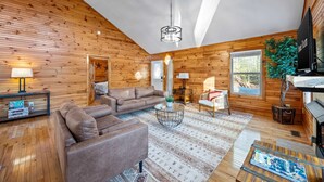 A cozy cabin interior with a wooden interior, a sofa, a coffee table, a lamp, and a television. - Cozy Cabin in Mountains Firepit Views Games (Sautee Nacoochee)