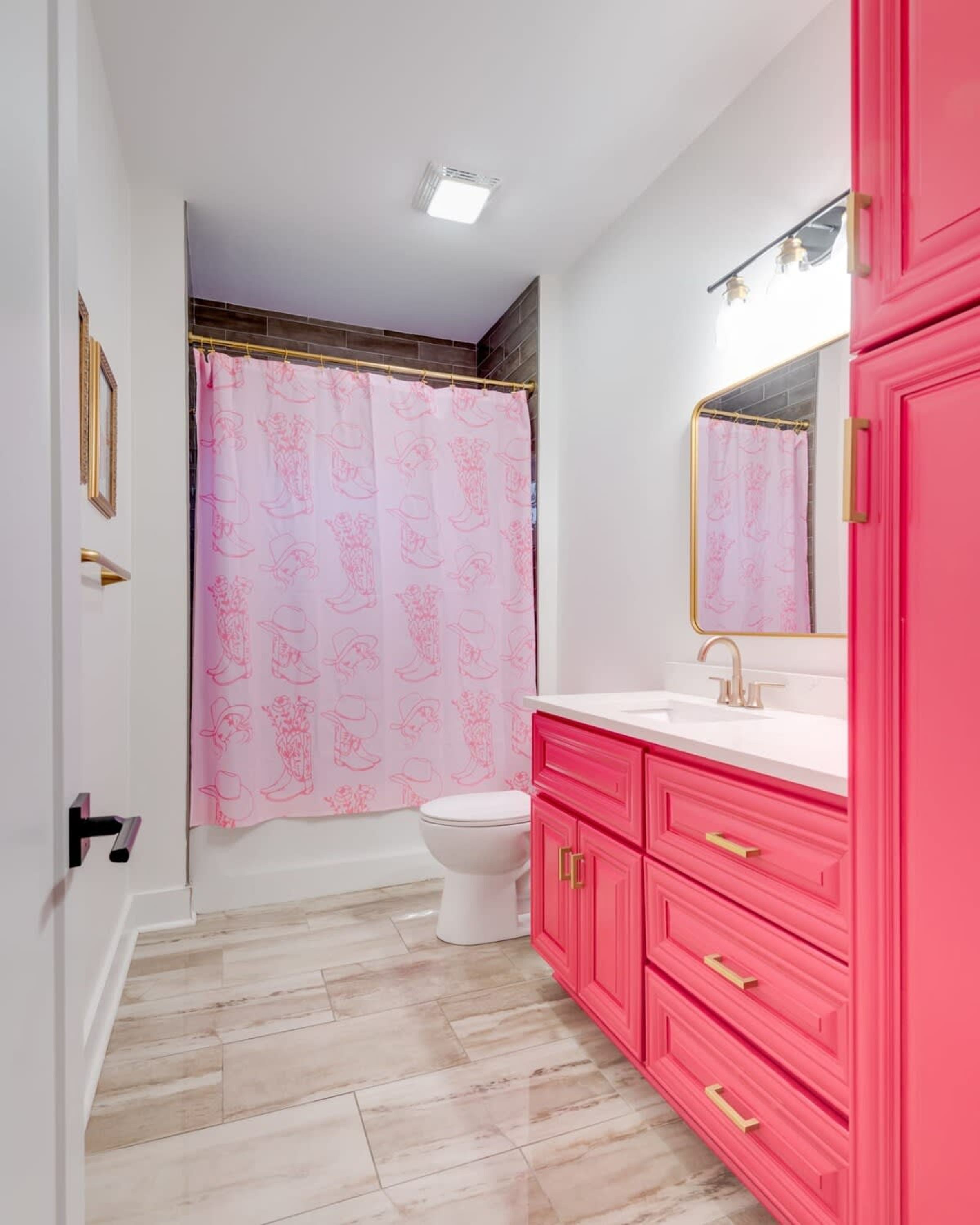 A bathroom with a white toilet, pink shower curtain, and pink vanity with gold handles.