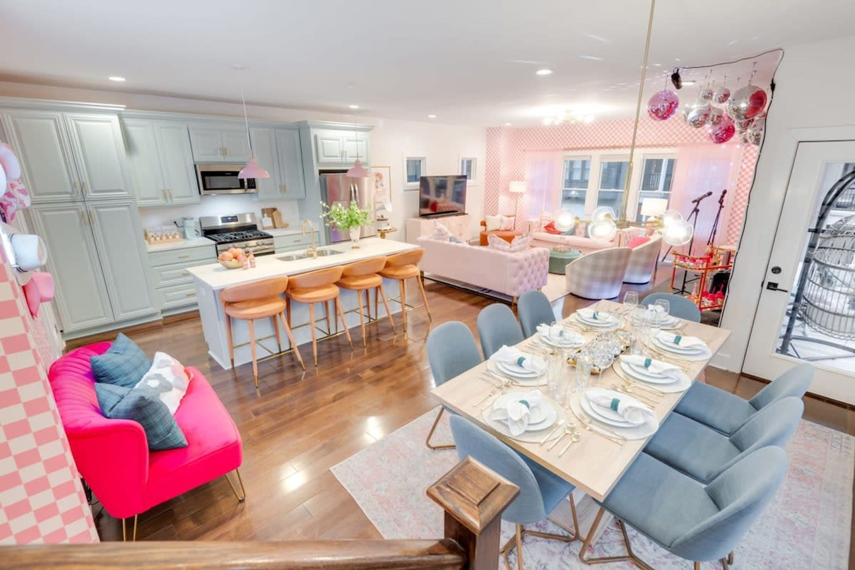 Una cocina moderna con una isla central, taburetes de bar, una mesa de comedor para seis personas y un sofá rosa.