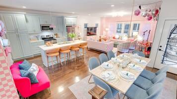 Una cocina moderna con una isla central, taburetes de bar, una mesa de comedor para seis personas y un sofá rosa.