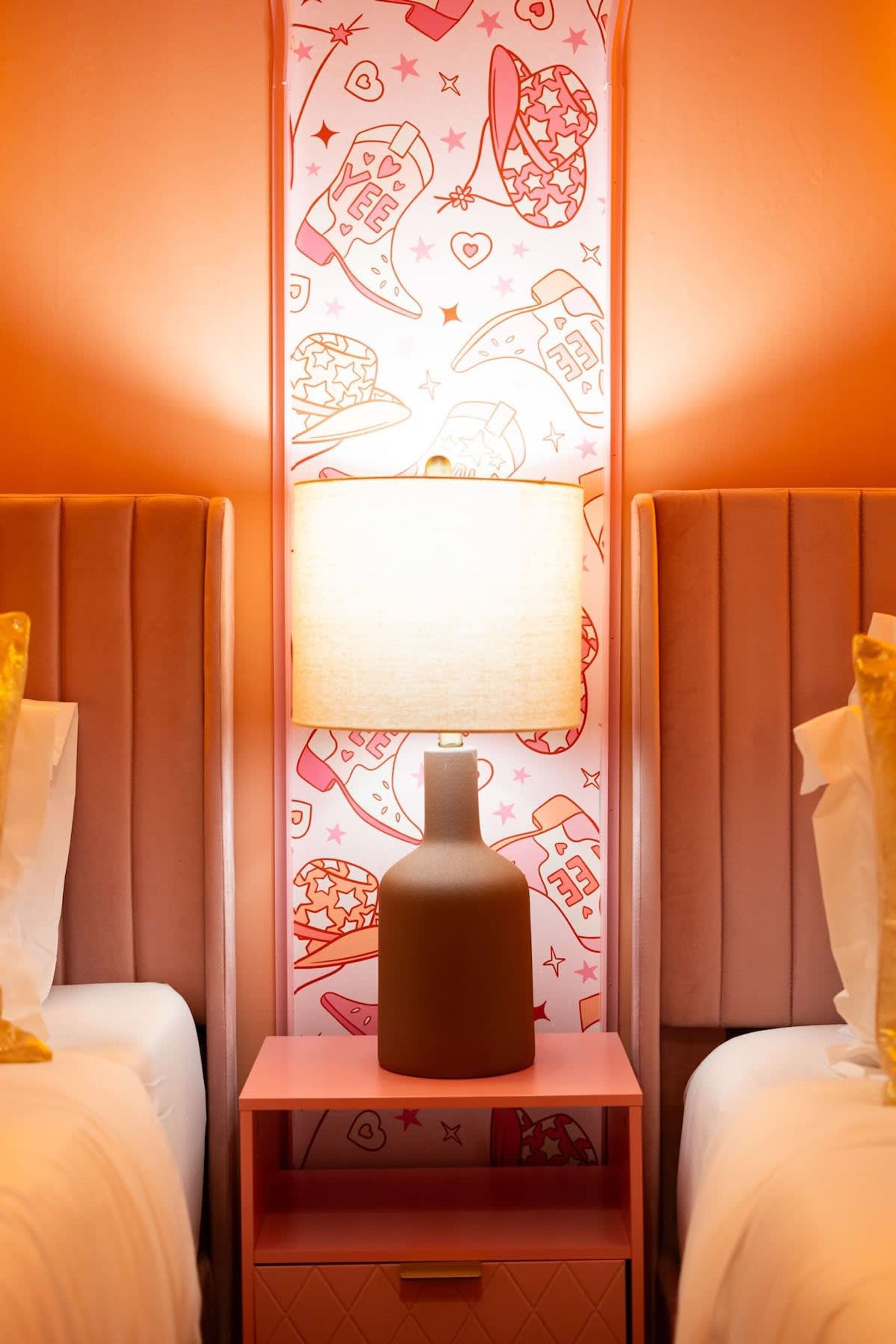 A hotel room with two beds, a nightstand with a lamp, and a wall with a pattern of stars and shapes.
