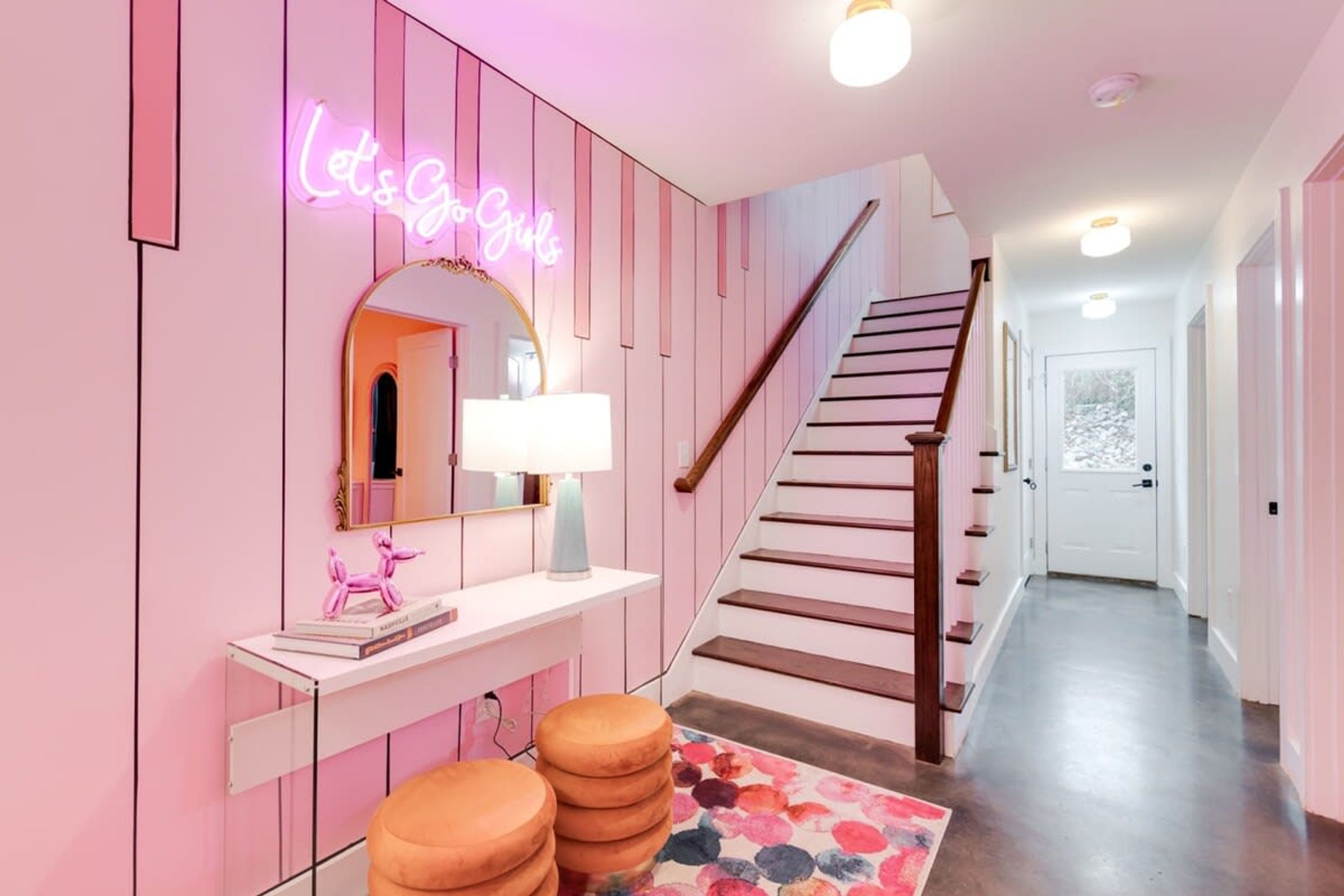 Un pasillo decorado en tonos rosas con un letrero de neón, una escalera y un espejo.