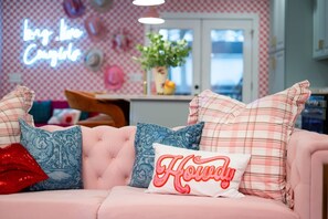 A pink sofa with patterned pillows and a neon sign in the background.