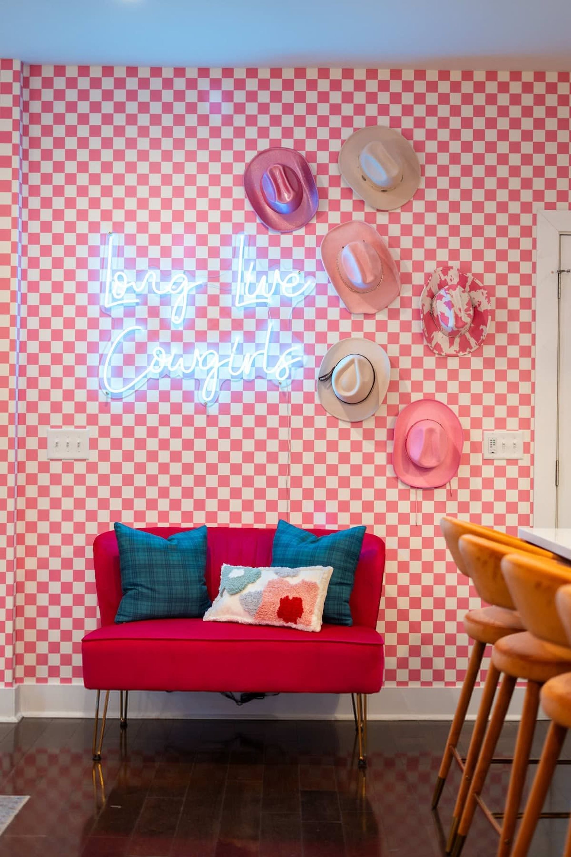 A room with a red sofa, a neon sign, and several hats on the wall.