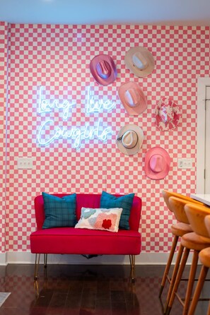 Una habitación con un sofá rojo, un letrero de neón y varios sombreros en la pared.