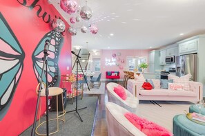 A modern living room with a pink sofa, a dining area with a pink and white checkered wall, and a kitchen with white cabinets. - Butterfly BNB - Unforgettable Nashville Experience (Nashville)