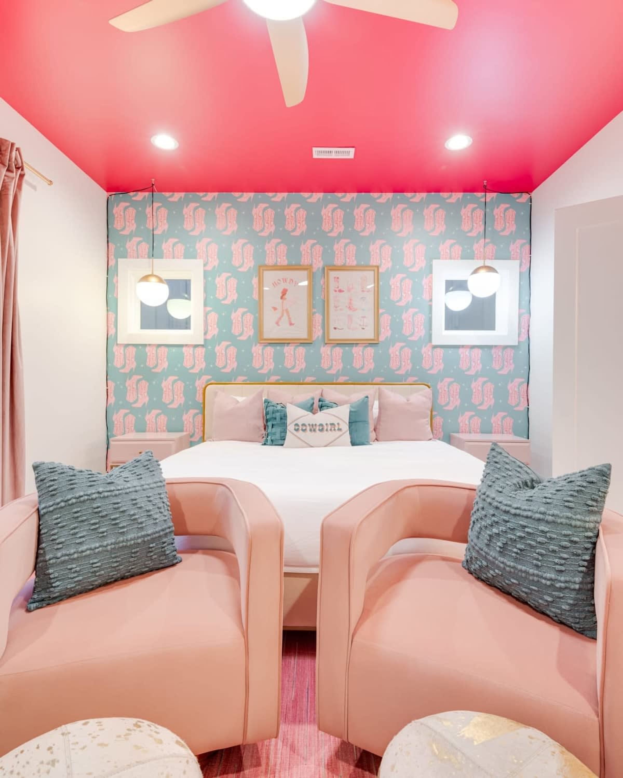 A bedroom with a bed, two chairs, a ceiling fan, and wall art.