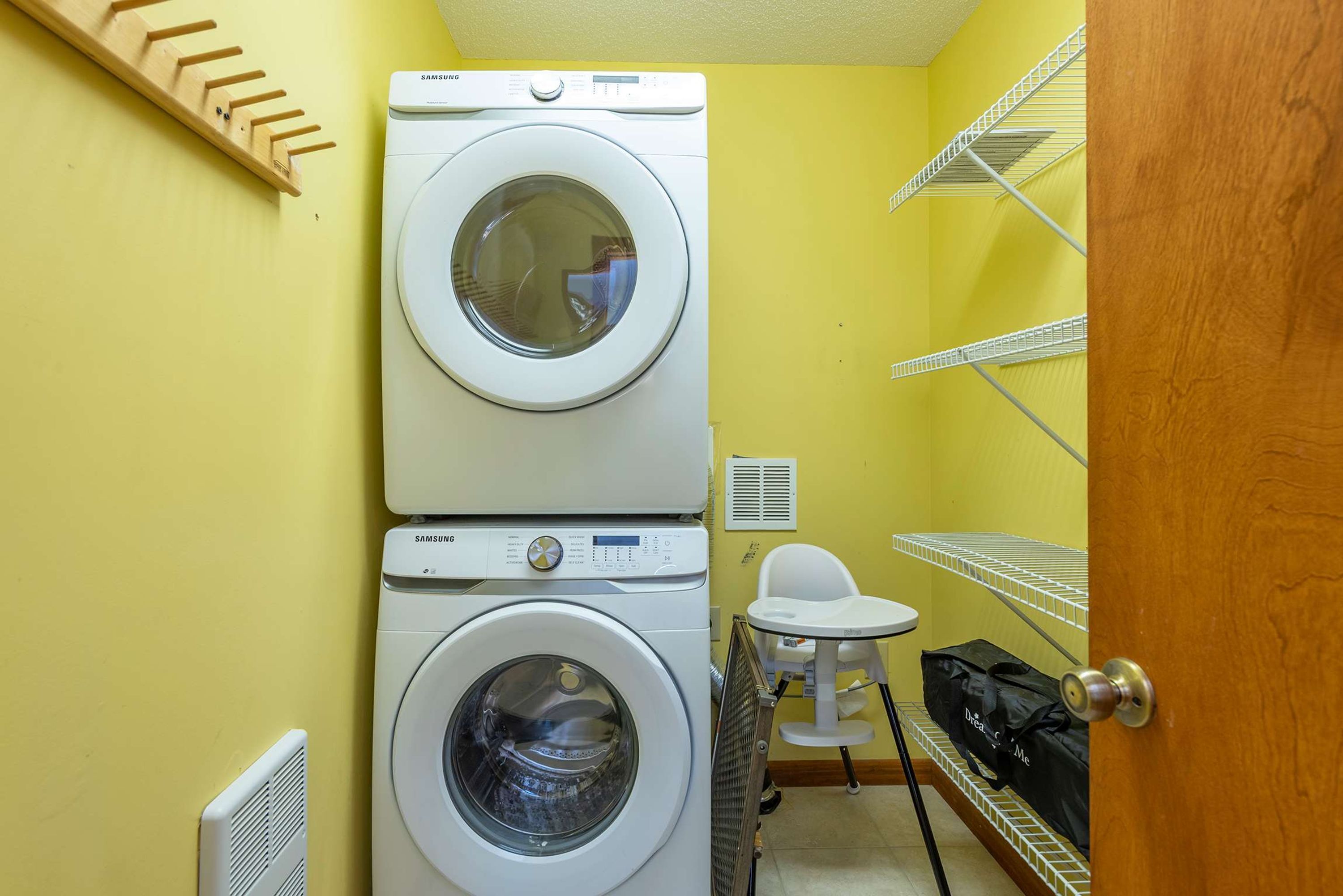 A laundry room with two stacked washers and dryers, a chair, and shelves with laundry baskets.