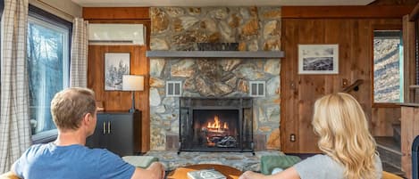 Un salón acogedor con chimenea de piedra, paredes de madera y vistas al exterior.