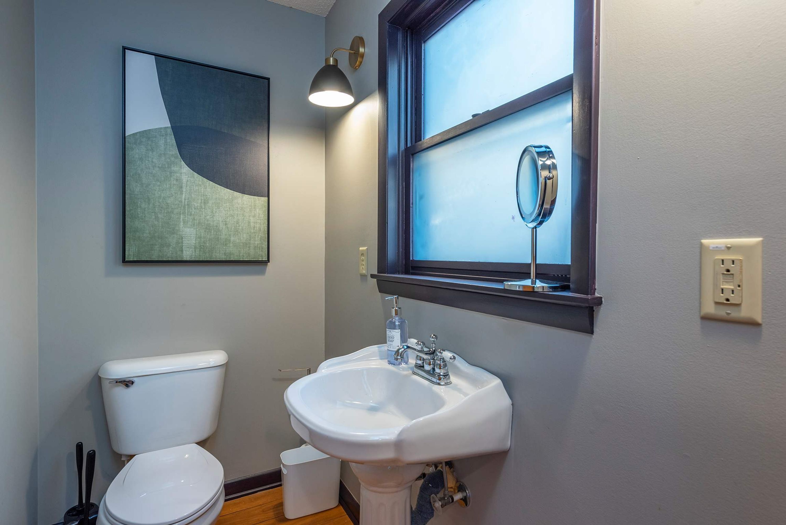 A bathroom with a toilet, sink, and a window with a mirror.