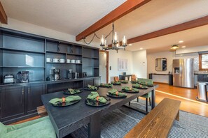 Uma sala de jantar moderna com uma mesa comprida posta para refeição, um espaço para café e uma cozinha ao fundo.