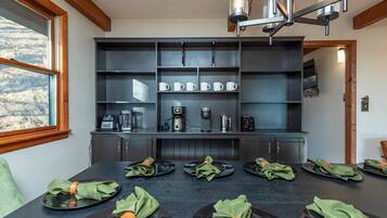 A modern kitchen with built-in appliances, a dining table set for six with green napkins, and a view of the outdoors through a window.