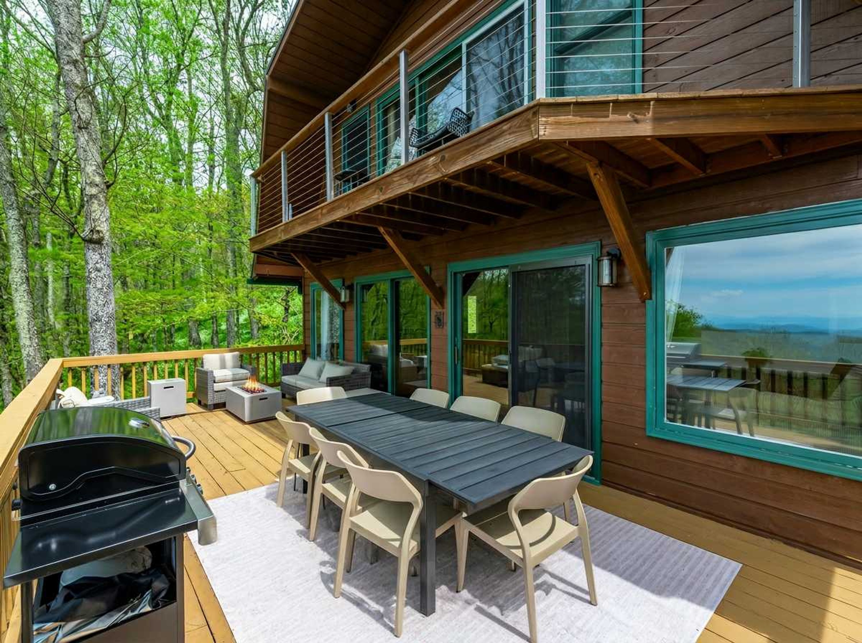 A wooden deck with a table and chairs, a grill, and a view of the forest.