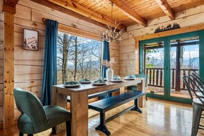 A wooden cabin interior with a dining table set for four, a bench, and a view of the outdoors through a door. - Luxe Mountain Escape - Fire Pit - Hot Tub - Sauna (Sevierville)