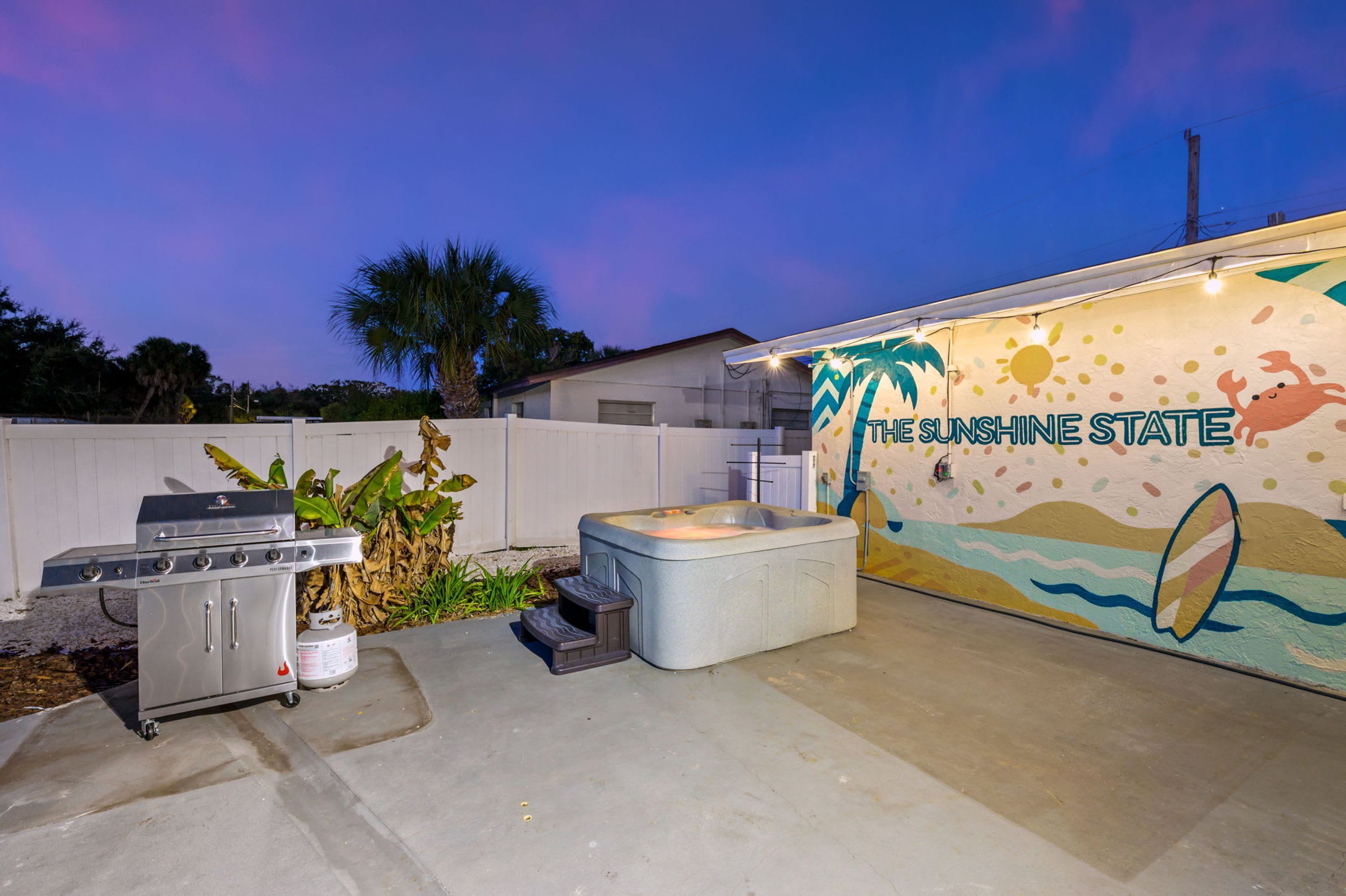 An outdoor patio area with a hot tub, a barbecue grill, and a wall mural with the text 'THE SUNSHINE STATE'.