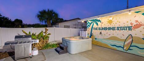 An outdoor patio area with a hot tub, a barbecue grill, and a wall mural with the text 'THE SUNSHINE STATE'.