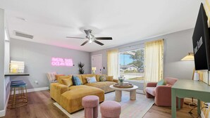 Uma sala de estar moderna com um sofá, pufes, uma mesa de centro e um ventilador de teto.