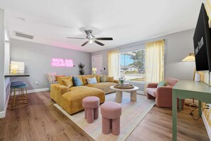 A modern living room with a sofa, ottomans, a coffee table, and a ceiling fan. - Pastel Palms - Sport Court - Pool - Hot Tub - Bar (Bradenton)