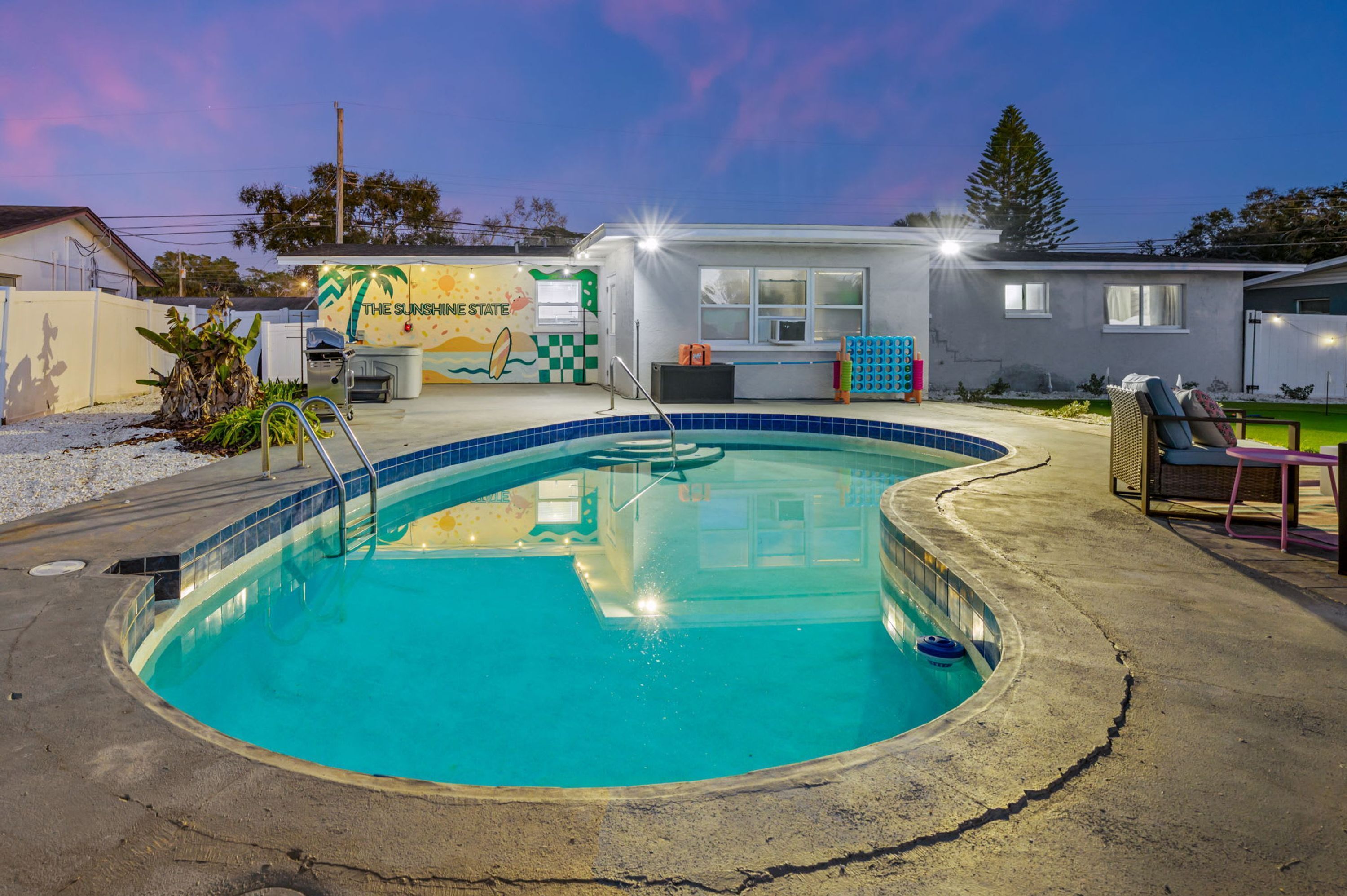 A swimming pool with a sun mural, a small building with a checkered wall, and outdoor seating.