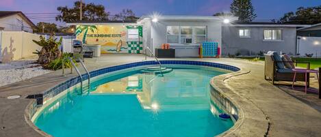 A swimming pool with a sun mural, a small building with a checkered wall, and outdoor seating.