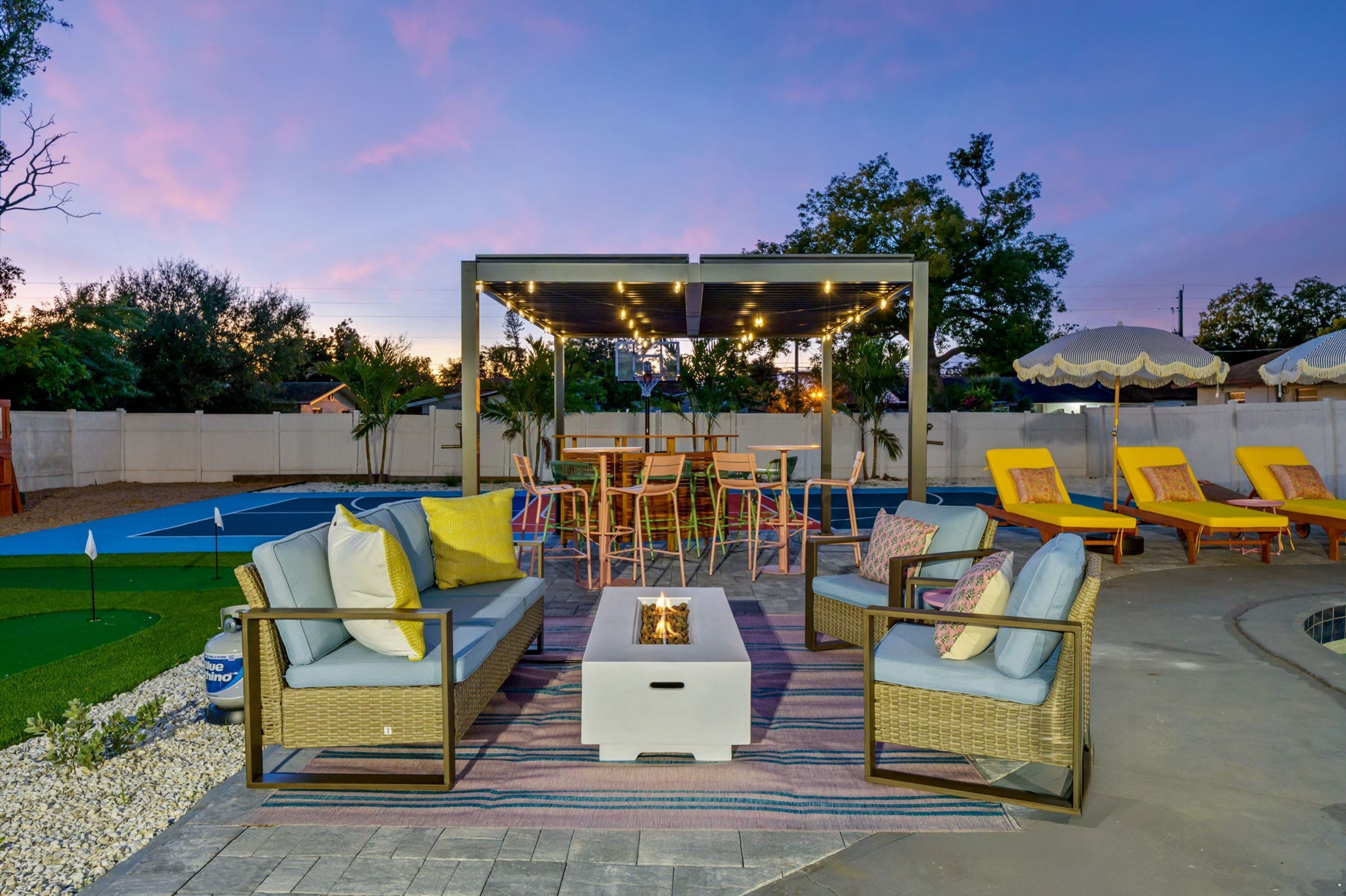 An outdoor patio with a pool, lounge chairs, a covered seating area, and a fire pit.
