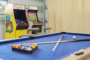 A pool table with billiard balls and cues, arcade machines, and a window with a view. - Pastel Palms - Sport Court - Pool - Hot Tub - Bar (Bradenton)