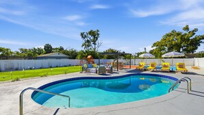 Piscina com borda azulejada, rodeada por espreguiçadeiras e guarda-sóis.