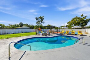 A swimming pool with a tiled edge, surrounded by lounge chairs and umbrellas. - Pastel Palms - Sport Court - Pool - Hot Tub - Bar (Bradenton)