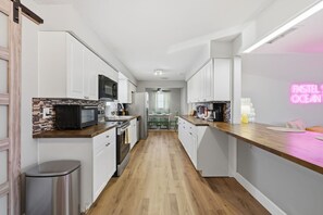 A modern kitchen with white cabinets, a wooden countertop, and a neon sign. - Pastel Palms - Sport Court - Pool - Hot Tub - Bar (Bradenton)