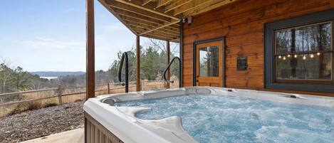 A hot tub under a wooden pergola with a view of the landscape.