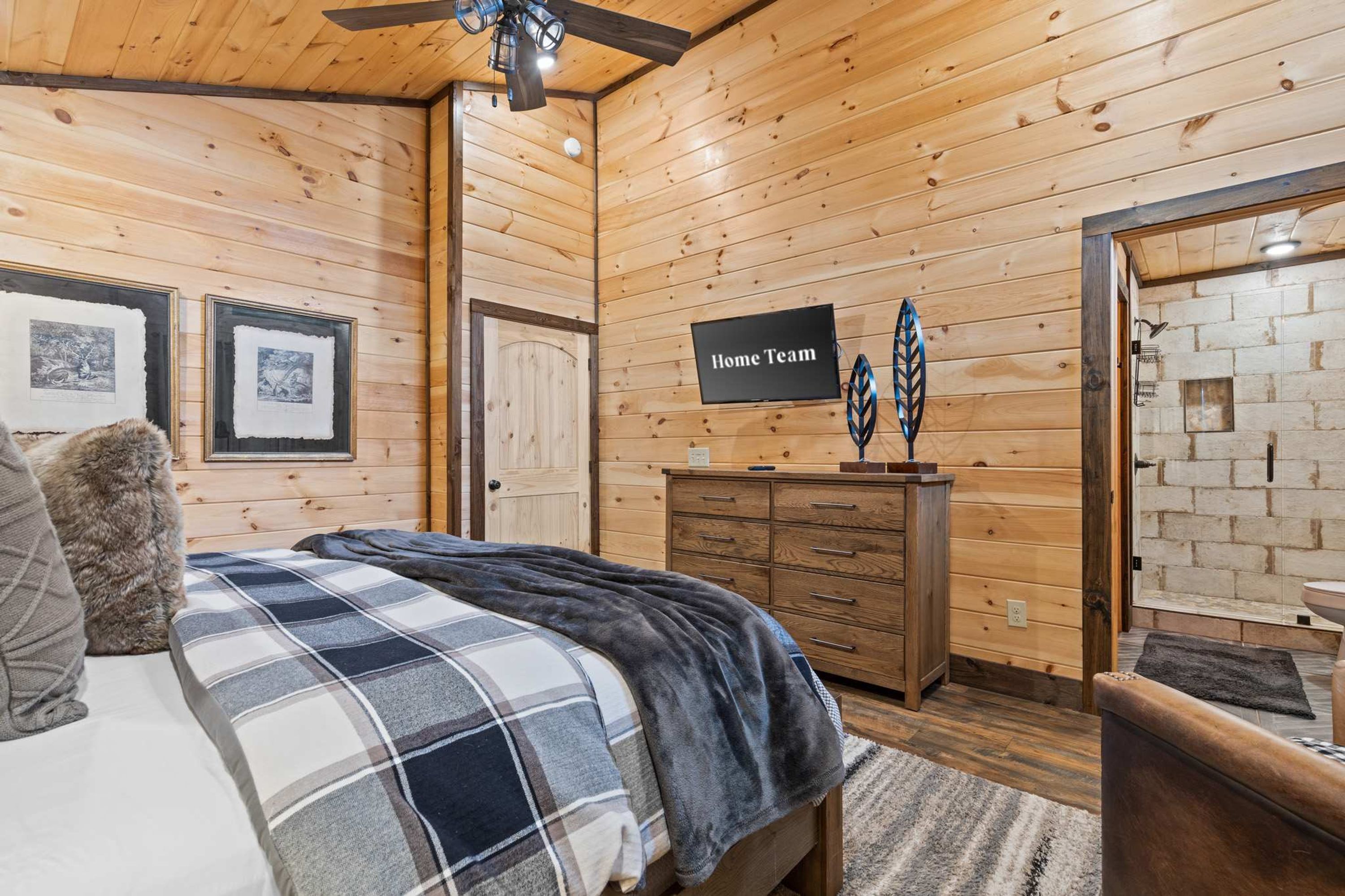 A cozy room with wooden walls, a bed with a plaid blanket, a dresser, and a sign that reads 'Home Team'.