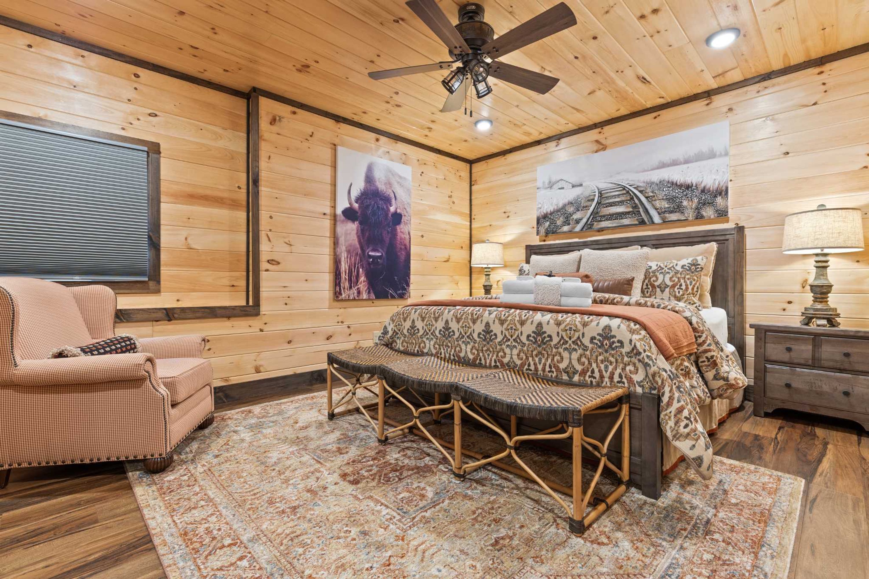 A cozy room with a bed, a chair, a bench, and a ceiling fan.