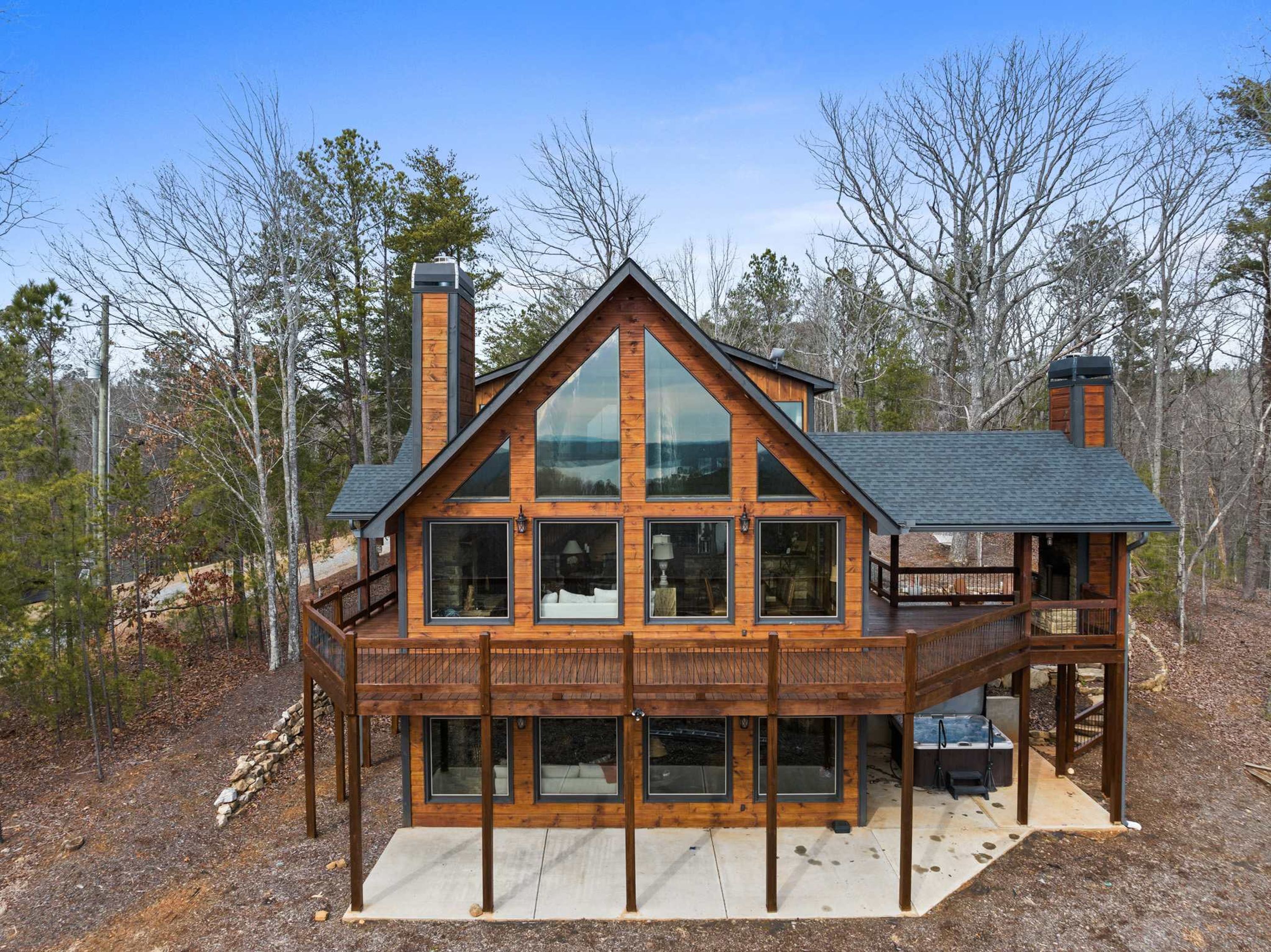 A modern log cabin with a large deck, multiple windows, and a chimney.