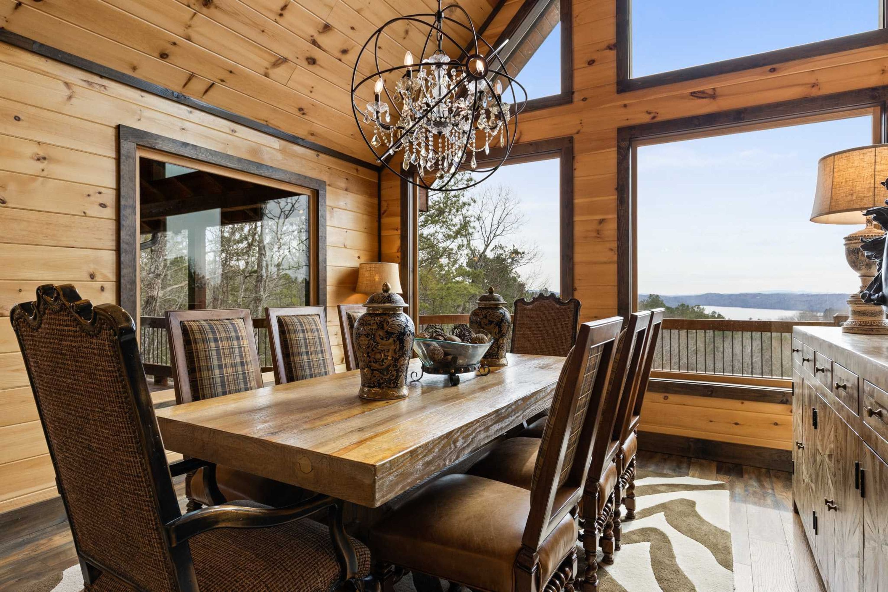 A wooden dining room with a chandelier, large windows, and a view of the outdoors.