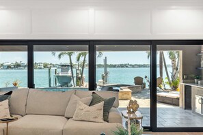 A modern living room with a large window overlooking a marina and water. - Harbor Villa Waterfront Pool Spa Firepit (Indian Rocks Beach)
