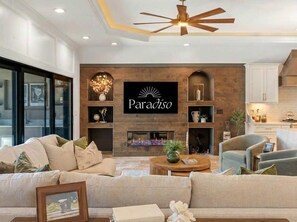 A modern living room with a fireplace, a mounted sign reading 'Paradiso,' and a ceiling fan. - Harbor Villa Waterfront Pool Spa Firepit (Indian Rocks Beach)