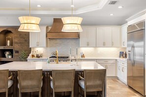 A modern kitchen with a central island, stainless steel appliances, and a stone backsplash. - Harbor Villa Waterfront Pool Spa Firepit (Indian Rocks Beach)