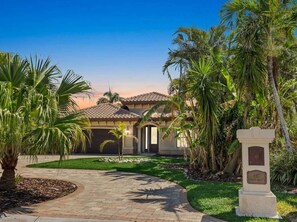 A residential property with a paved driveway, palm trees, and a well-maintained lawn. - Harbor Villa Waterfront Pool Spa Firepit (Indian Rocks Beach)