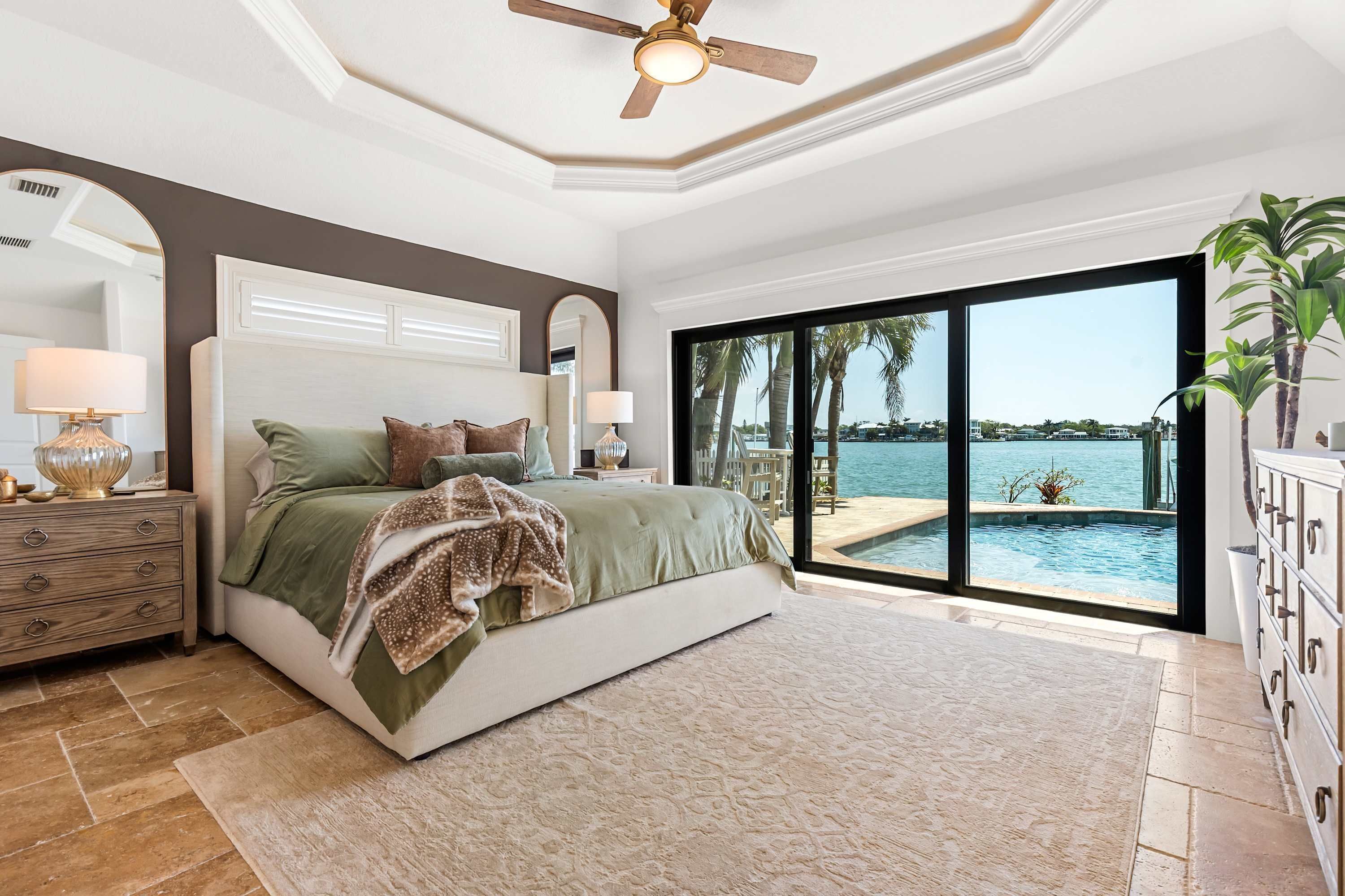 Quarto com cama grande, mesa de cabeceira, cômoda, ventoinha no teto e vista para a piscina e oceano.