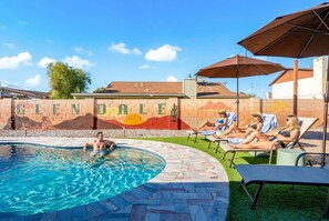 Ein Swimmingpool mit Wandmalerei, Liegestühlen und Sonnenschirmen.
