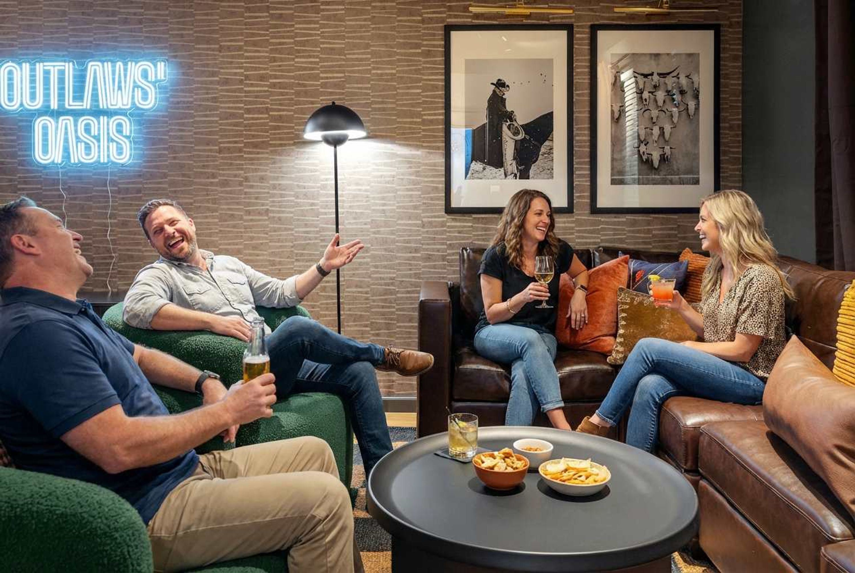 Eine Gruppe von Personen sitzt auf einer Couch in einem Raum mit Backsteinwand, einer Neonreklame und gerahmten Bildern.