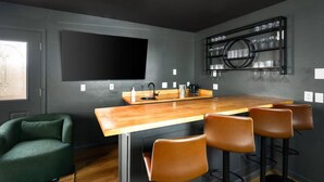 A modern kitchen with a wooden island, bar stools, a large flat-screen TV, and a wine rack. - Epic Family Getaway Speakeasy Pool Basketball (Glendale)