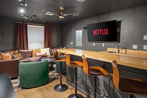 Ein modernes Wohnzimmer mit Barbereich, einer Ledersofa und einem großen Flachbildfernseher, der 'NETFLIX' anzeigt.